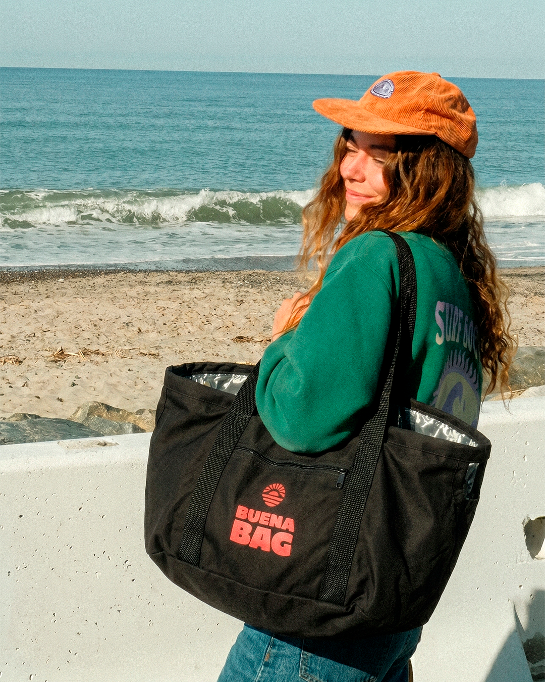 Garota de boné laranja com a Buena Bag no mar